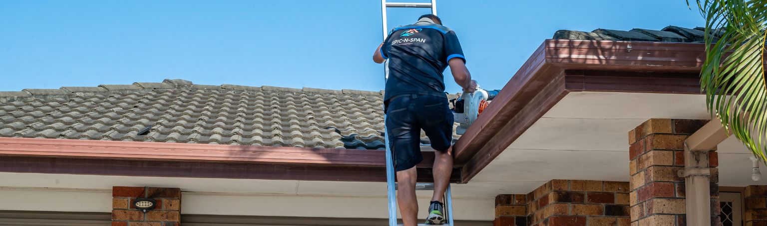 Spic N Span worker on a ladder clearing the roof gutters