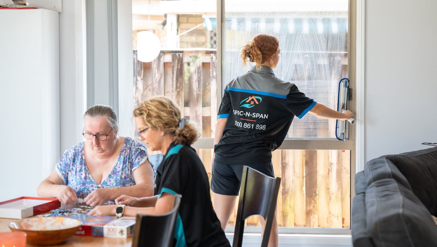 Spic N Span cleaner tidying up while a participant does a jigsaw puzzle at the dining table